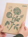Notebook with floral design and RHS logo held by hands on a light background
