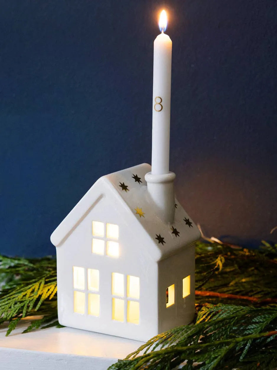 A ceramic house candle holder with numbered advent candles, designed to mark the countdown to Christmas.