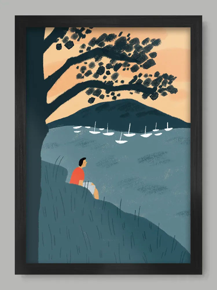 Framed artwork of a person sitting by a lake with sailboats and a tree.