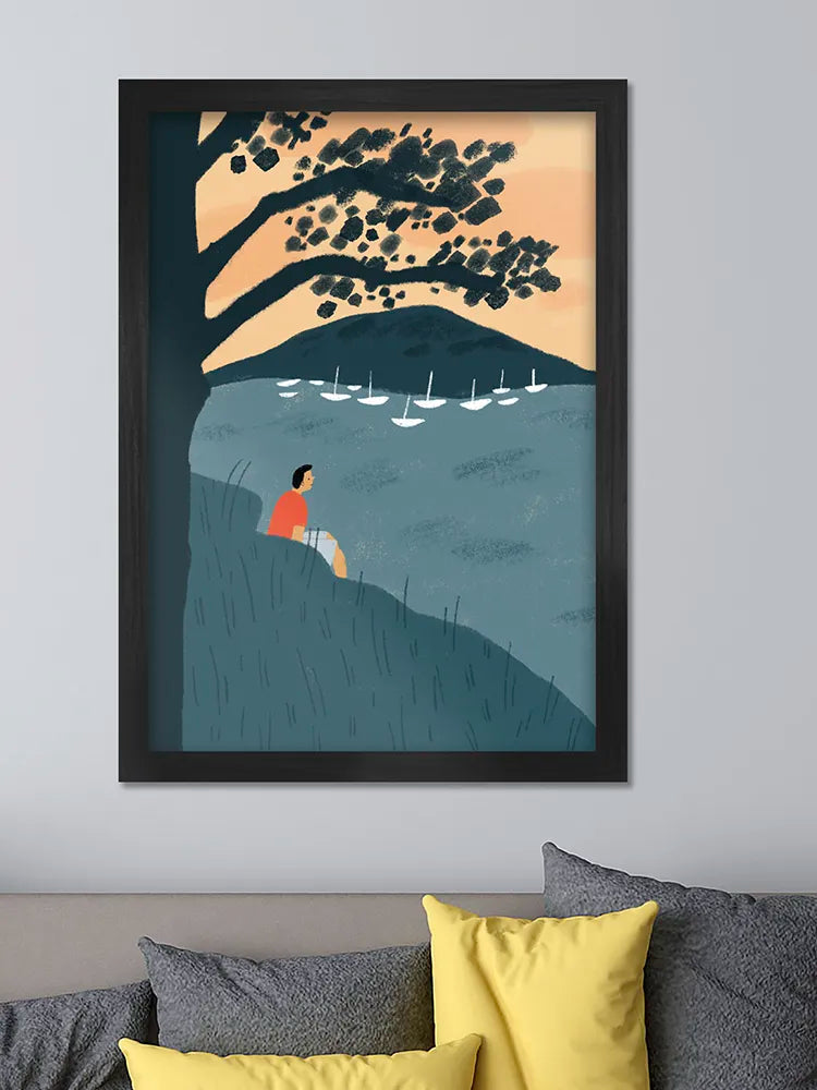 Framed artwork of a person sitting by a lake with sailboats under a tree, on a wall above a sofa.
