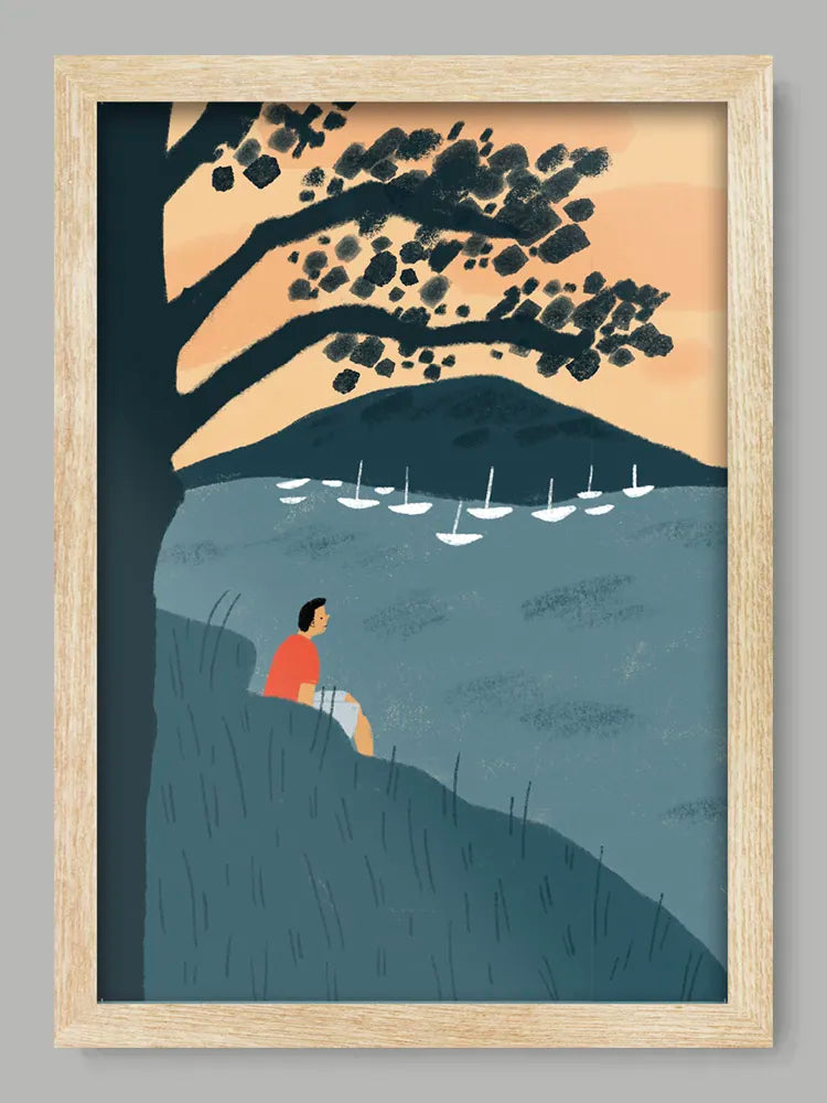 Framed artwork of a person sitting by a lake with sailboats and trees.