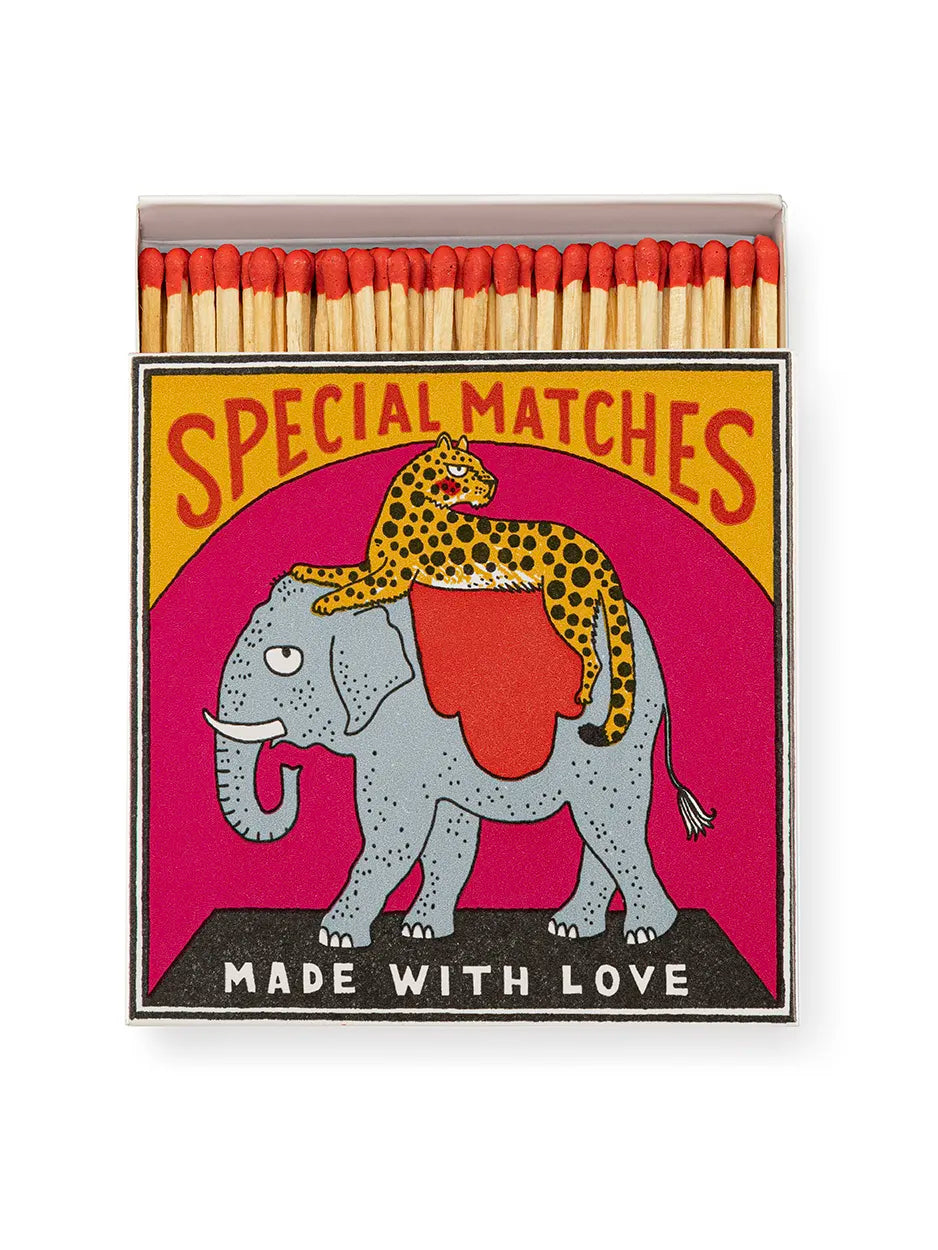 Square matchbox featuring an elephant with a cheetah lying on its back and the words 'Safety Matches, Made With Love.' Striking in every sense – these matchboxes are filled with 125 matchsticks ready to spark a little joy. Designed to add character to coffee tables, mantelpieces, and gift drawers, each box is a blend of function and flair.