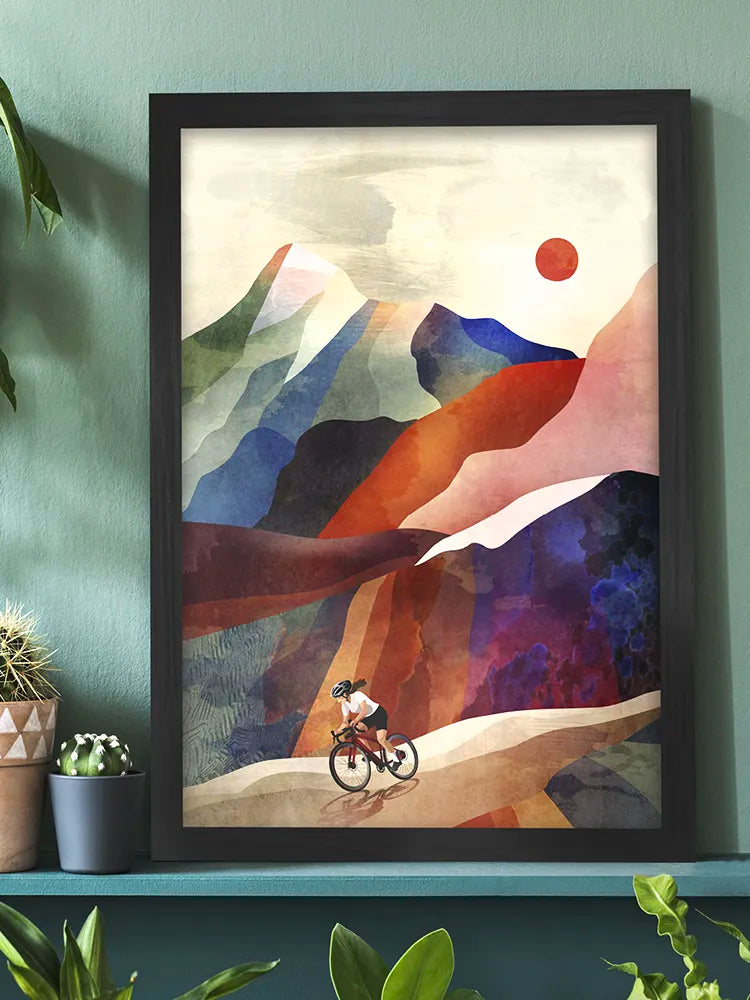 Framed abstract artwork of a cyclist on a mountain path with a colorful mountain landscape.