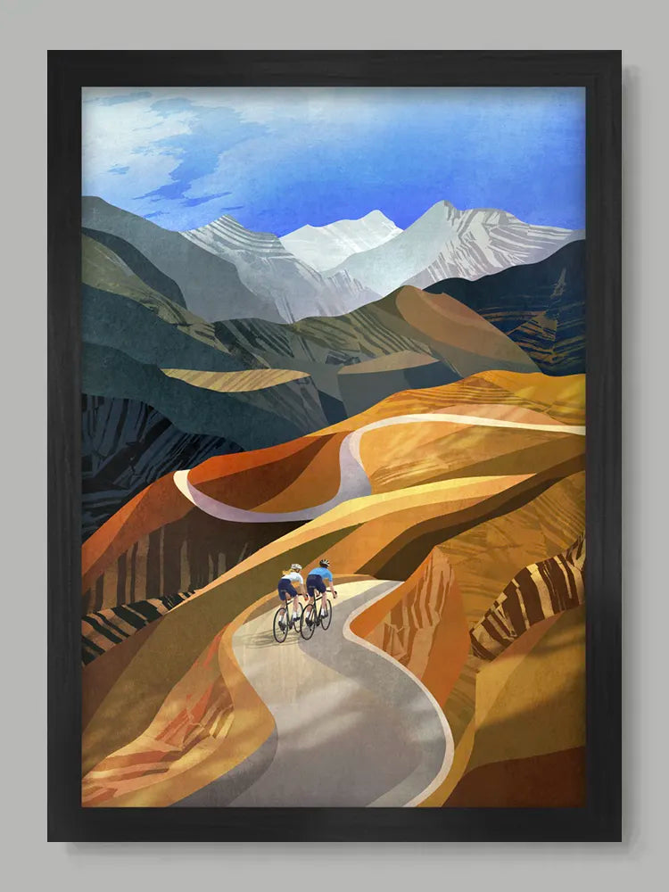Framed artwork of two cyclists on a mountain road with a mountainous landscape.