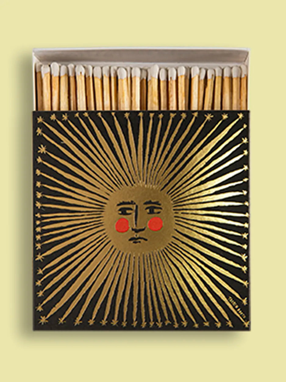 Square matchbox featuring a gold foil sun with an illustrated face and rosy red cheeks. Tabby Booth . Striking in every sense – these matchboxes are filled with 125 matchsticks ready to spark a little joy. Designed to add character to coffee tables, mantelpieces, and gift drawers, each box is a blend of function and flair.