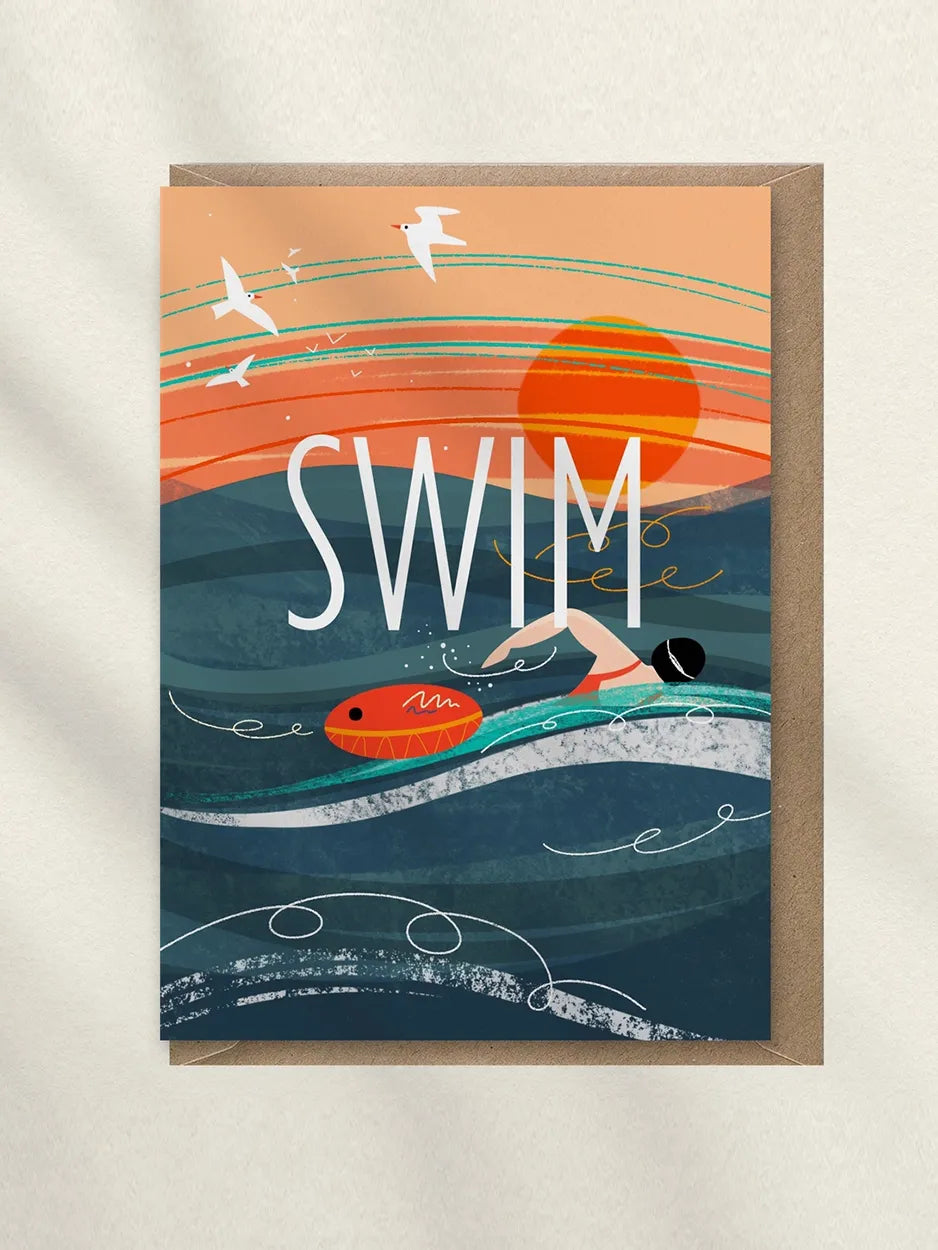 A square greeting card with a kraft envelope, featuring an illustrated ocean scene with a swimmer, surfboard, birds, and the word “SWIM” in large white letters.