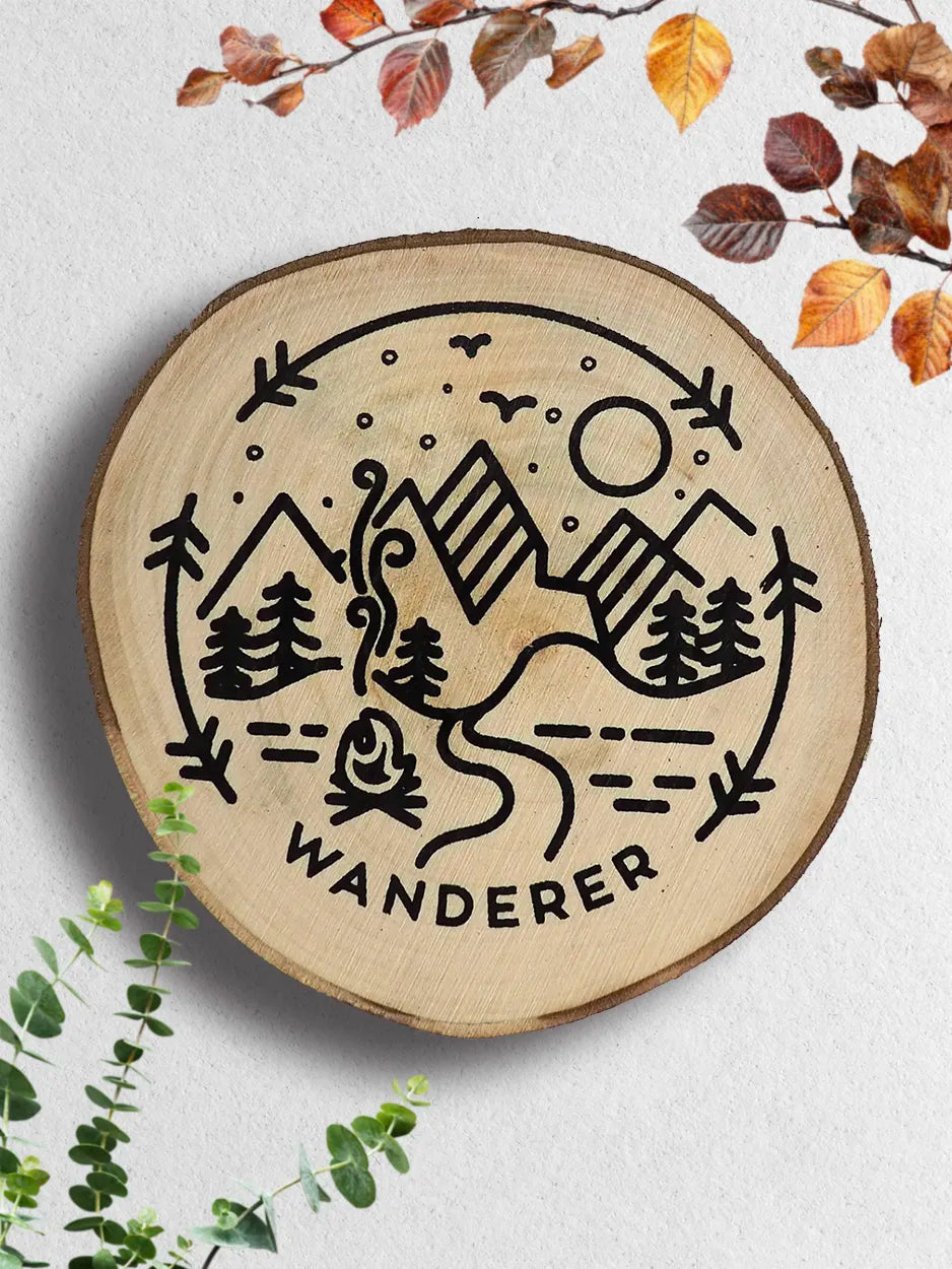 Wooden round sign with mountain and nature-themed design and 'Wanderer' text, surrounded by autumn leaves and greenery.